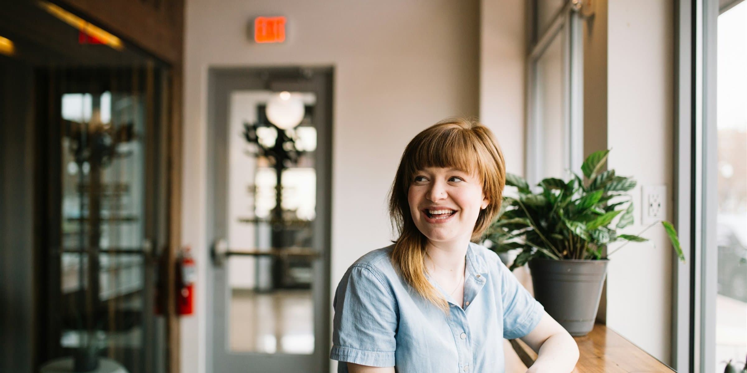A person leaning on a window counter in a bright room, laughing at something off-camera.