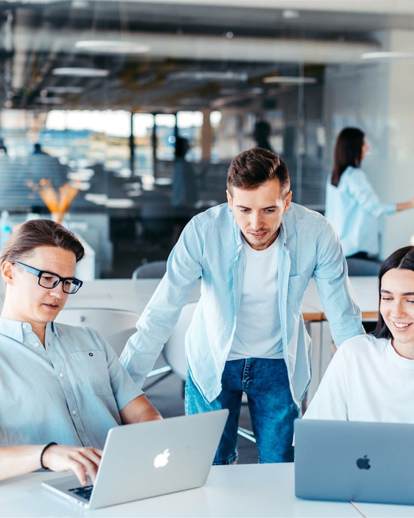 Three people at one desk looking at a shared screen, one of them leaning in to point at it.
